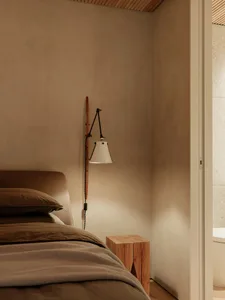 A minimalist bedroom with a plaster wall, a wooden bedside table, and a bed with brown bedding.