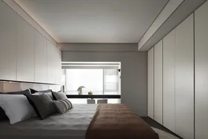 A modern minimalist bedroom with a bed, windows, and white cabinets.