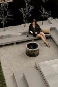 A modern residential outdoor area with a concrete fireplace, bench, and small trees.