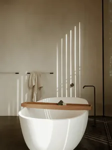 A minimalist white concrete bathroom with a freestanding bathtub, a wooden tray, and a towel rack.