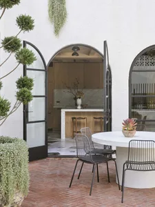 Modern outdoor patio area with brick floor, white stone table, and metal chairs.