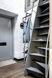 Modern staircase with a steel frame and gray carpet tiles leading to a door with a metal handle.