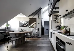 A modern minimalist kitchen interior with sleek, white cabinetry, dark wood floors, and a round dining table.