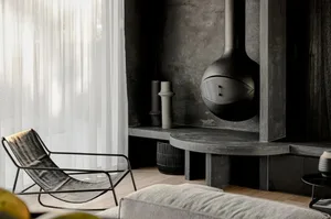 A modern minimalist living room featuring a concrete fireplace and a lounge chair in front of a large window with sheer white