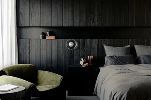 A minimalist bedroom with dark wooden walls, a green armchair, and a bed with grey bedding.