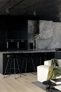 A minimalist residential kitchen showcasing a marble countertop and backsplash, with black stools and sleek black cabinetry.