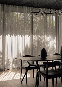 A modern dining room featuring a wooden table and chairs with sheer curtains and a chandelier.