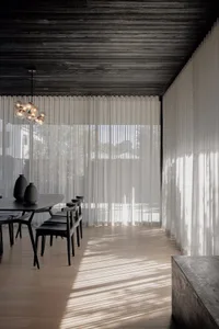 A minimalist residential room featuring white curtains, glass walls, and concrete furniture.