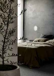 A minimalist bedroom featuring a concrete wall and bed with olive green bedding.