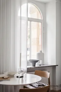 Minimalist kitchen featuring a white marble table and chairs, with minimalist decorations on a window sill.