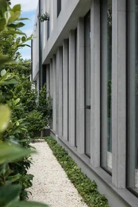Modern building exterior featuring concrete columns, glass windows, and gravel pathway.