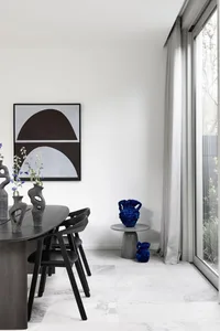 A modern minimalist dining room featuring black furniture, a geometric abstract painting, and decorative vases.