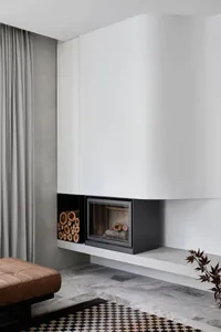 Modern minimalist living room with concrete fireplace, checkered rug, and leather ottoman.