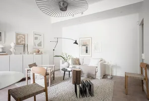 A modern minimalist living room with neutral-toned furniture and decor, featuring a white sofa, wooden chairs, and a black an