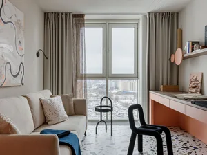 A minimalist apartment interior featuring a white couch, beige curtains, and a terrazzo floor.
