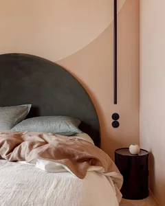 A minimalist bedroom with a gray upholstered headboard, soft textiles, and a sleek side table against a pastel wall.