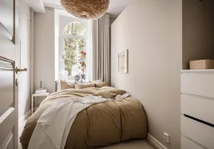 A minimalist bedroom with a bed covered in beige textiles and a floating light fixture above it.