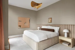 A minimalist bedroom with a white upholstered bed, beige upholstered headboard, and modern white table lamps.