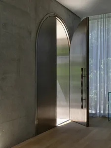 A minimalist entrance with an arched metal door in a modern interior design setting.