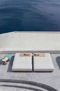 Minimalist outdoor lounging area with cushioned seats, marble tiles, and a glass table.