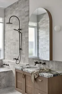 A modern bathroom featuring marble countertops and concrete elements, with an arched mirror above the vanity.