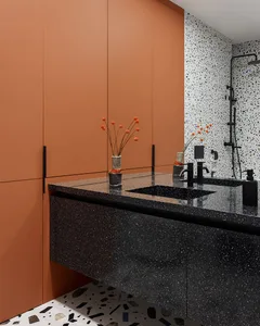 Modern bathroom with black terrazzo countertop, sink, and orange floral arrangement.