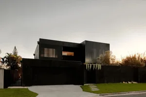 A modern black house with metallic accents and a green lawn in the foreground.