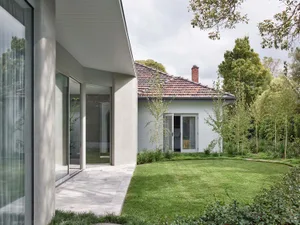 Modern-style exterior residential backyard with concrete patio and grass lawn, featuring a white house with a red roof and br
