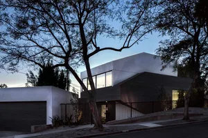 A modern concrete house with large windows and a black fence.