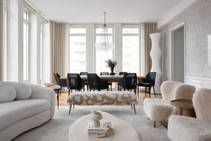 A modern living room with white and beige furniture, large windows, and a large coffee table with a vase and books.