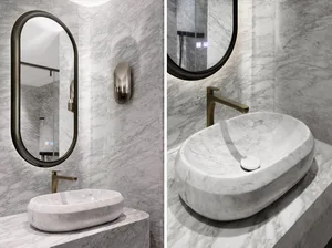 A sleek, modern bathroom with marble accents, featuring an oval-shaped sink and a wall-mounted faucet.