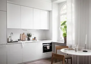 A white minimalist kitchen with white cabinets, a sink, an oven, and green plants.