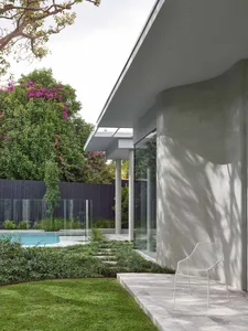 A modern residential backyard featuring concrete surfaces and a white chair on a patio.