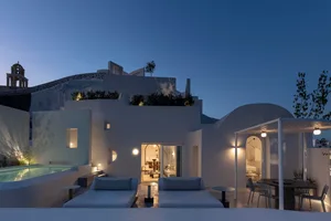 Modern residential patio with white plaster walls and night lighting, featuring a sitting area with lounge chairs and a dinin