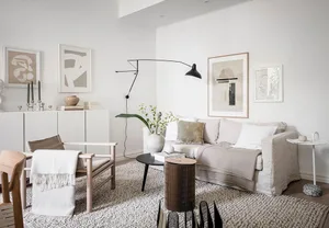 A modern, minimalist living room featuring a neutral-colored couch, black floor lamp, and white-framed abstract art.