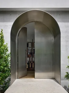A metallic doorway with a curved archway, open, revealing a glimpse of a bookshelf inside.
