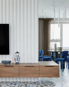 A modern living room with a terrazzo floor, blue chairs, and a wooden floating cabinet.