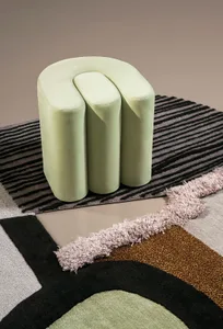 A modern, green leather stool with abstract, striped rug underneath.