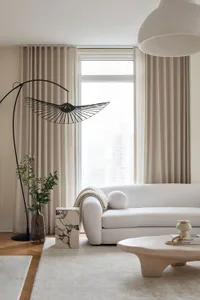 A modern, minimalist living room with a white sofa, neutral curtains, and a sleek, metal floor lamp.