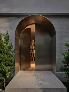 An arched, metallic entrance with a concrete base, leading to a warmly lit interior.
