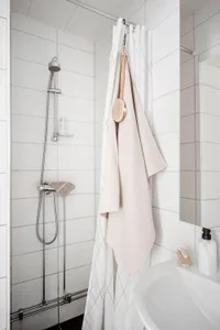 A minimalist bathroom with white ceramic tiles, a shower, a towel rack, and a sink.