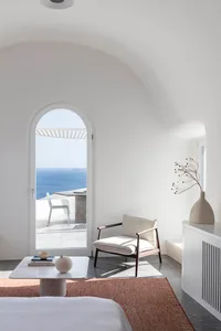A minimalist living room with white walls and furniture, featuring a comfortable lounge chair with a cushion, a small round t
