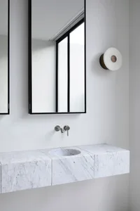 A modern minimalist bathroom with a marble countertop and sink, a large mirror, and a window with a white frame.