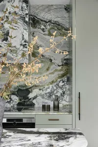 Modern kitchen with marble walls, countertops, and sink, featuring stainless steel appliances and green plants.