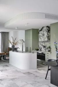 Modern residential kitchen featuring a large island with marble countertop and green cabinets, complemented by concrete floor
