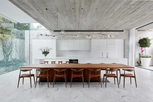 Modern minimalist kitchen with marble countertops and cabinets, featuring a large wooden dining table and chairs.