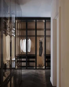 Modern minimalist closet with glass doors and clothing items hanging neatly.