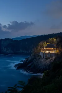 A modern residential house built on a rocky cliffside with concrete walls and wooden accents.