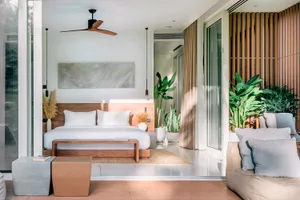 A modern bedroom featuring a concrete floor, minimalist decor, and a cozy seating area with greenery.