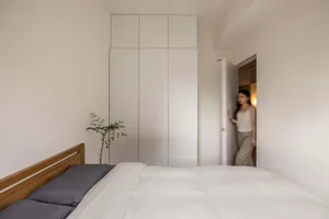 A minimalist bedroom featuring white wooden furniture and white walls.